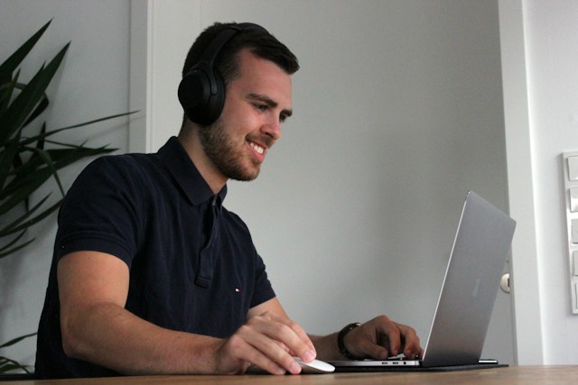 Man wearing headphones playing on a laptop while smiling